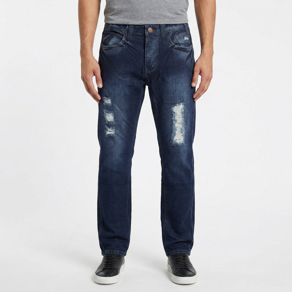 A model wearing dark blue distressed ETRN denim jeans with ripped details on the thighs, paired with a gray t-shirt and black sneakers.