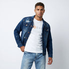 A male model styling the ETRN distressed indigo denim jacket over a white graphic t-shirt and light blue jeans for an edgy, premium streetwear look.