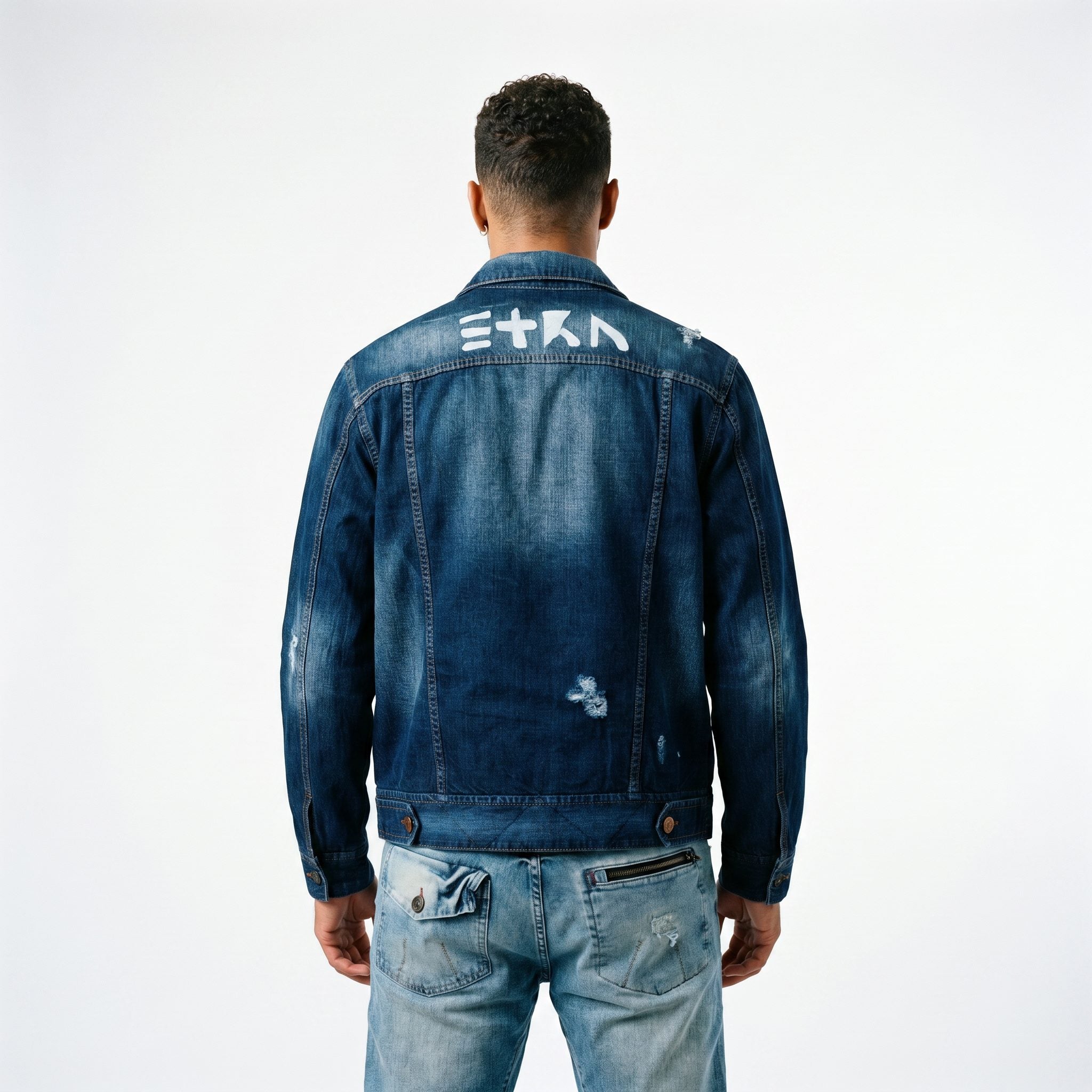 A male model viewed from behind wearing the ETRN distressed indigo denim jacket with brand name 'ETRN' printed across the shoulders and light-wash blue ETRN jeans, for an edgy, premium streetwear look.