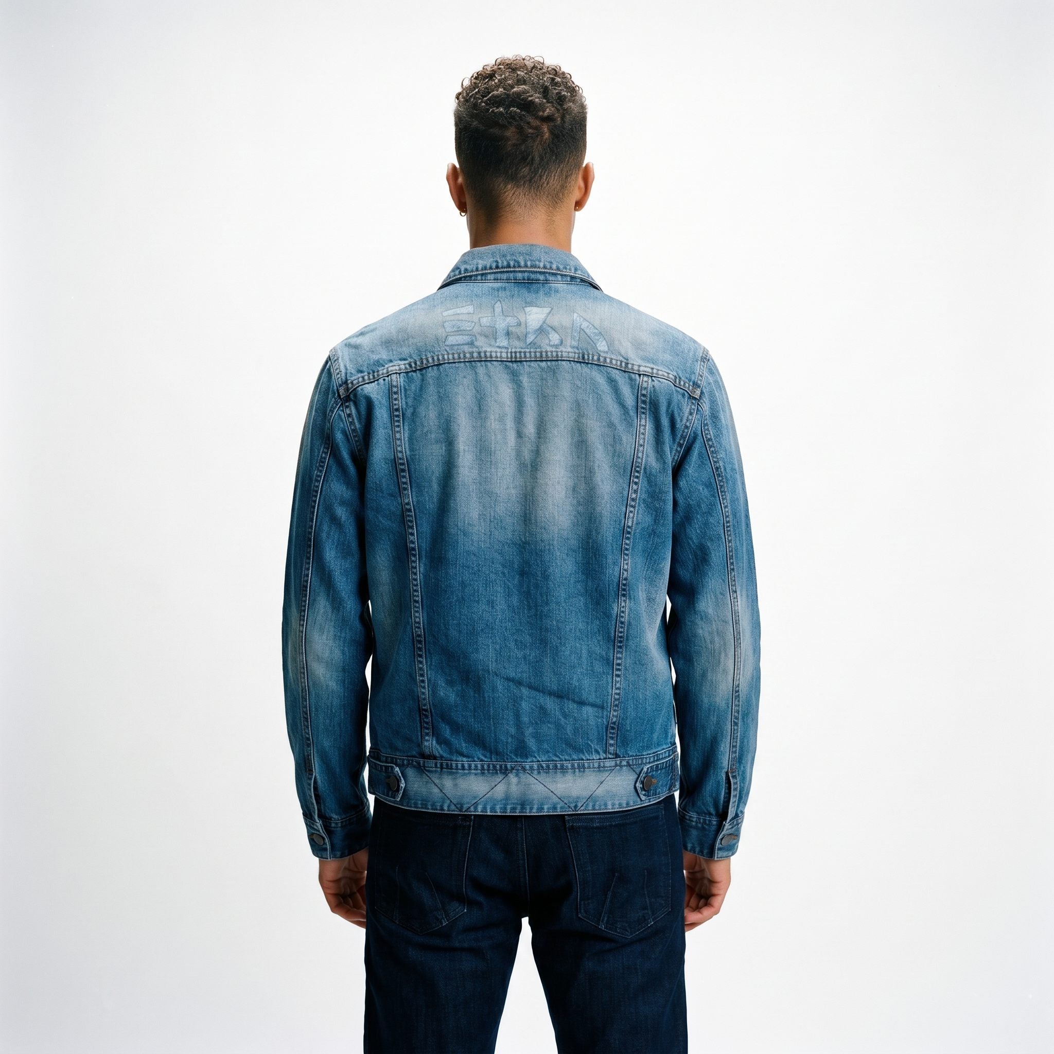 A male model viewed from behind wearing the ETRN engineered denim jacket with brand name 'ETRN' printed across the shoulders and dark blue ETRN jeans, for an edgy, premium streetwear look.