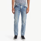 A model wearing light-wash blue ETRN denim jeans with a faded wash, paired with a gray t-shirt and black sneakers, shown from the waist down.